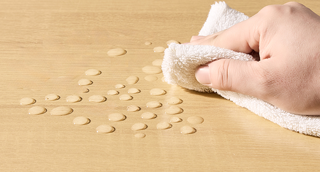 Utilisez à la main un chiffon blanc pour essuyer les gouttelettes d'eau sur la surface lisse du bois, démontrant ainsi les propriétés de résistance à l'eau ou faciles à nettoyer du matériau