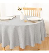 Ensemble de table à manger ronde avec nappe gris clair, assiettes blanches et chaise en bois visible, créant un décor de table minimaliste.