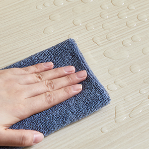 Essuyer à la main un parquet de couleur claire avec un chiffon en microfibre bleu. Gouttelettes d'eau visibles à la surface.