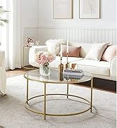 Intérieur du salon avec canapé blanc, table basse circulaire dorée, accents roses et art mural encadré. Vase de fleurs sur table.