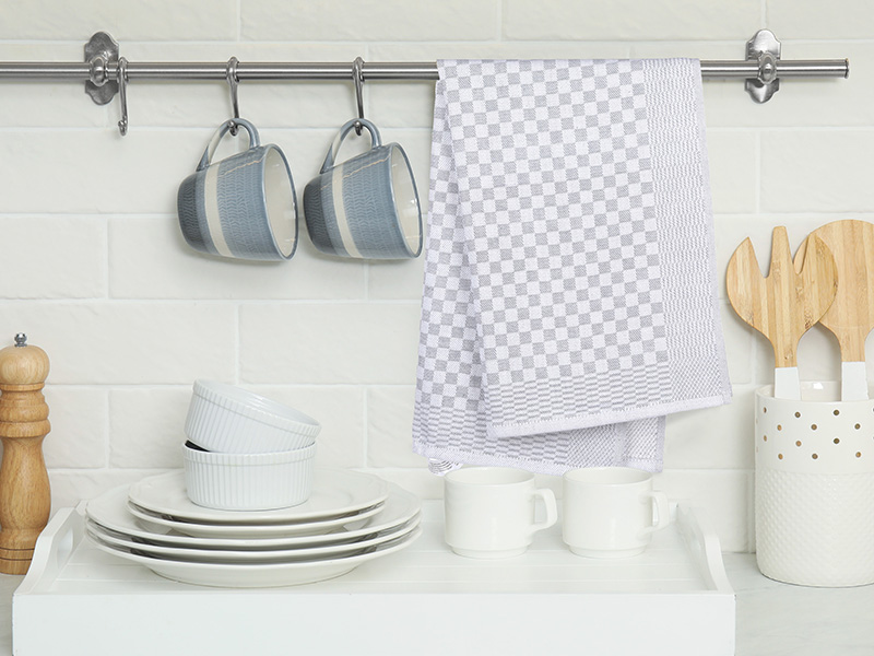 Configuration de l'organisation murale de la cuisine avec une tige métallique montée retenant des tasses bleues, un torchon à carreaux et divers ustensiles de cuisine sur des carreaux blancs