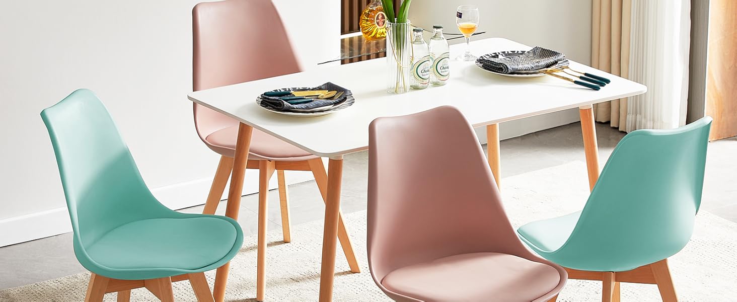 avec table rectangulaire blanche et quatre chaises. Deux chaises roses et deux chaises bleu sarcelle avec pieds en bois. Table dressée pour un repas.