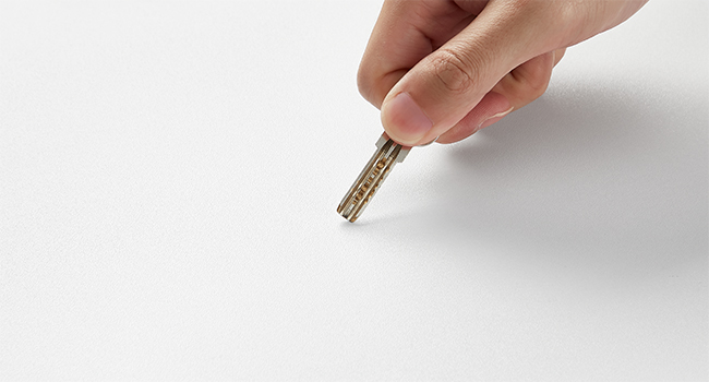 Main tenant une clé argentée sur fond blanc, démontrant un mouvement d'insertion ou de retrait.