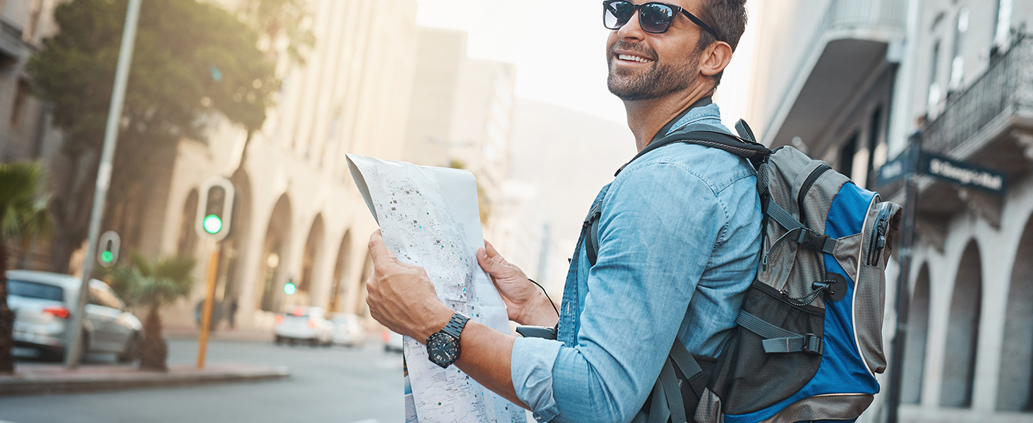Touriste avec sac à dos bleu debout dans la rue de la ville, tenant et regardant un appareil électronique ou une carte.
