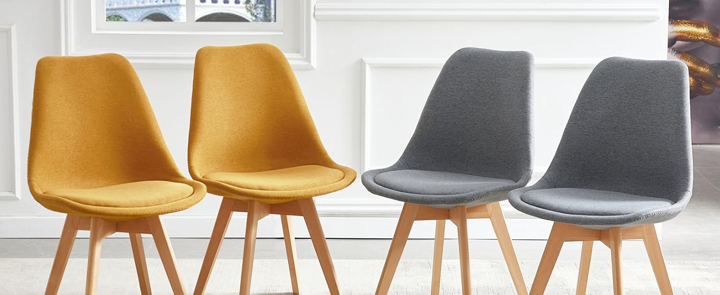 Quatre chaises de salle à manger modernes avec revêtement en tissu, deux jaunes et deux grises, avec pieds en bois. Situé sur un intérieur blanc avec des œuvres d'art murales décoratives et une vue sur la fenêtre.