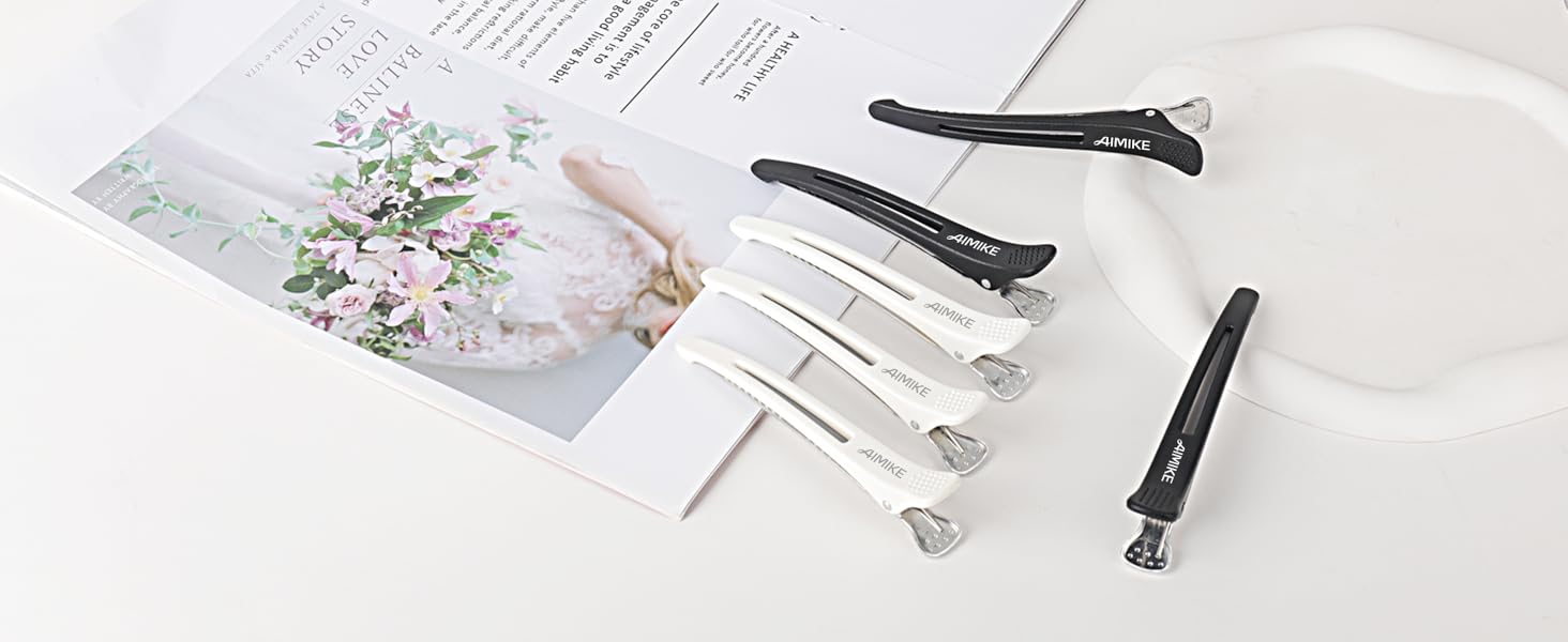 Collection de pinces à cheveux affichées sur une surface blanche, y compris des pinces crocodile noires et blanches et des épingles décoratives, avec une image florale en arrière-plan