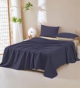 bleu marine posée sur un lit dans une pièce lumineuse à la décoration minimaliste, comprenant un drap-housse et un drap plat.