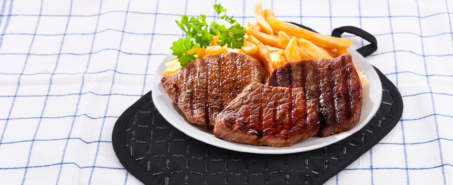 Assiette avec bifteck grillé, frites et laitue sur une nappe à carreaux. Le bifteck présente des marques de gril visibles. Servi sur un napperon noir texturé ou sur une plaque chauffante