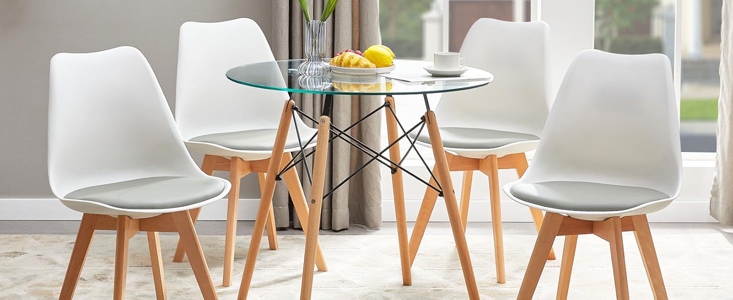 avec table ronde en verre et quatre chaises blanches avec pieds en bois. Cette chambre lumineuse est dotée de grandes fenêtres et d'éléments décoratifs.
