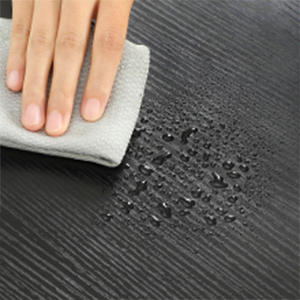 Essuyer à la main une surface en bois foncé avec un chiffon, démontrant des propriétés de résistance à l'eau ou à l'eau.